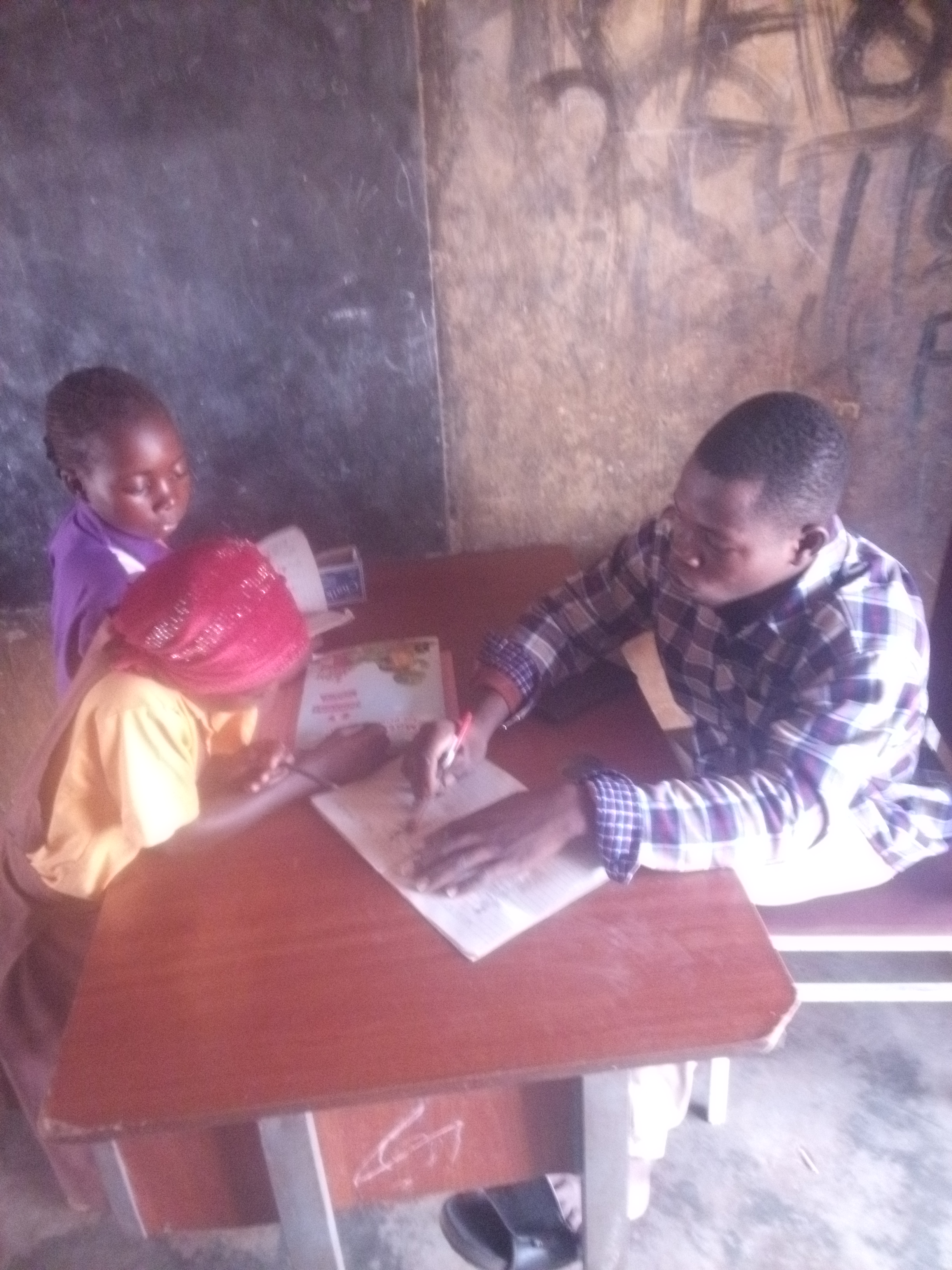 A teacher assists a pupil with reading in a Ghanaian primary school classroom.